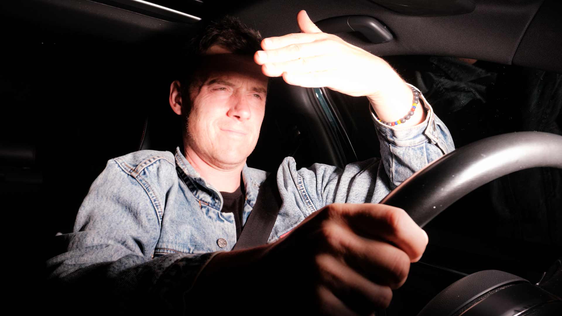 A driver shielding their eyes from intense oncoming headlight glare