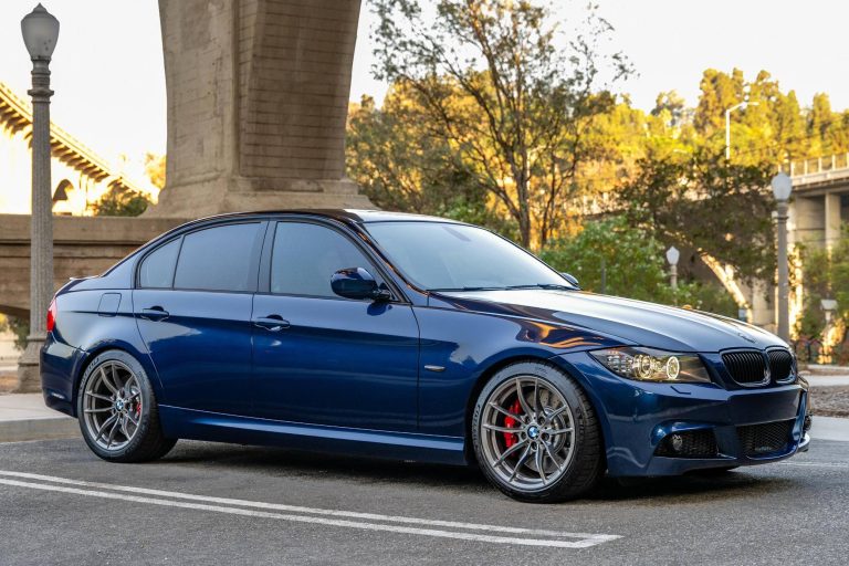 A dark blue BMW sedan parked outdoors near a bridge pillar on an asphalt street