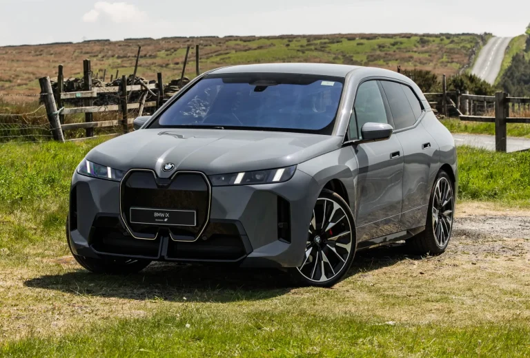 A BMW iX is standing on the grass near a shack