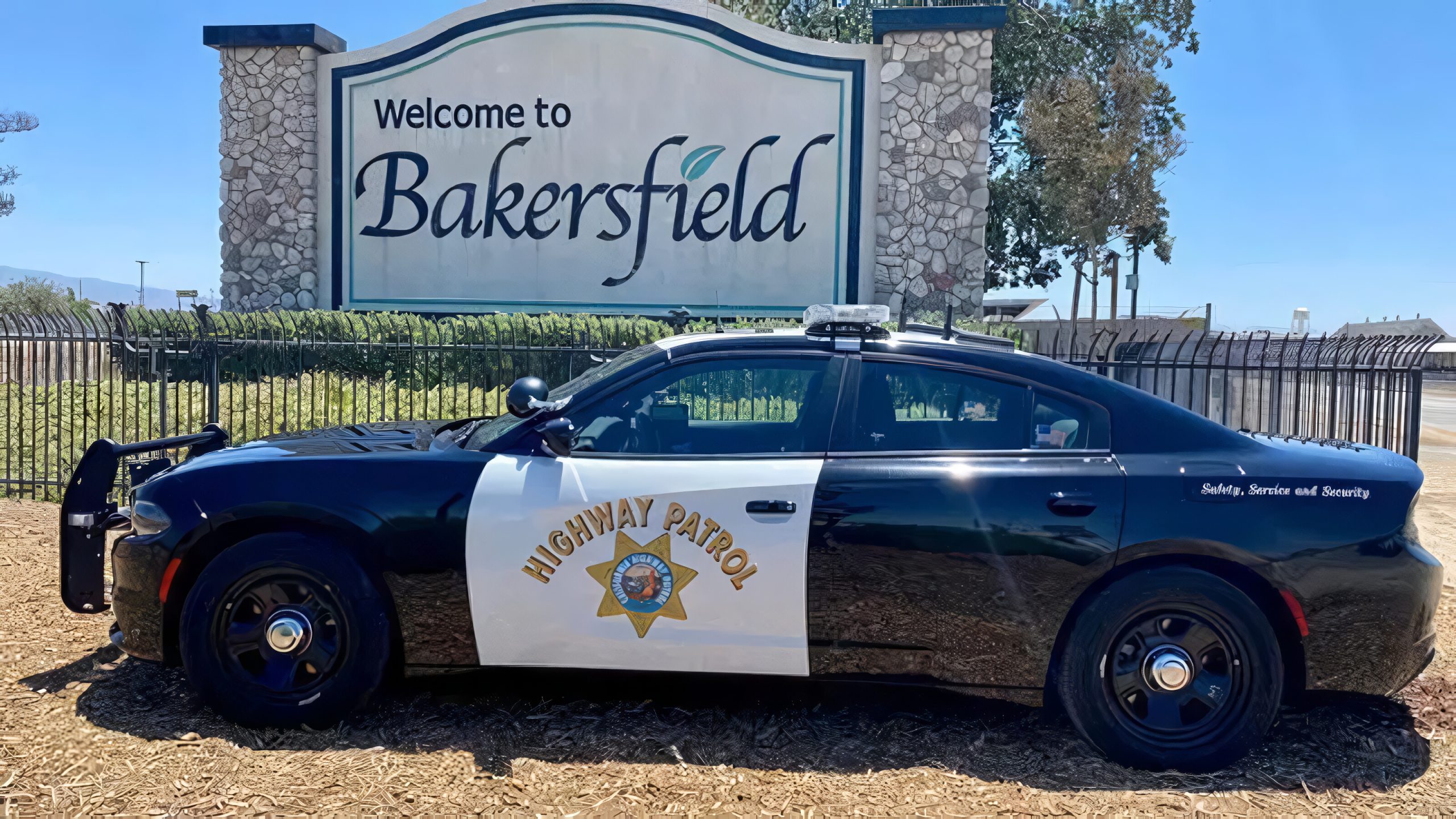 black and white California Highway Patrol car parked in front of a Bakersfield sign