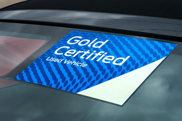 A blue and white Gold Certified Used Vehicle sticker attached to a car window