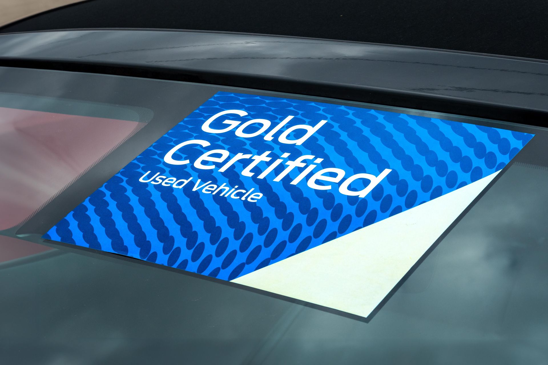 A blue and white Gold Certified Used Vehicle sticker attached to a car window
