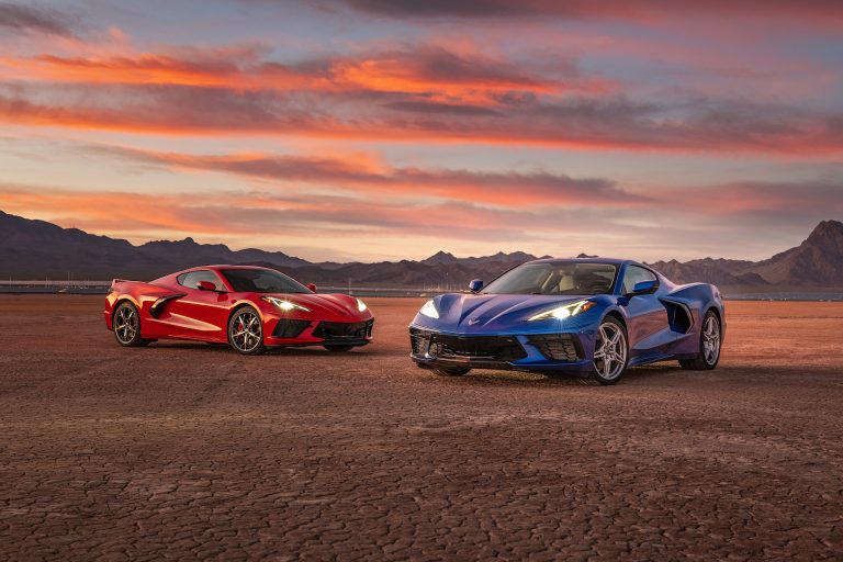 A red and a blue Chevrolet Corvette C8 parked outdoors during a scenic sunset