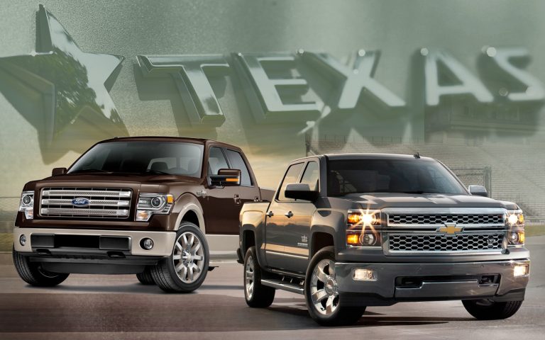 Two pickup trucks parked in front of a background featuring the word Texas