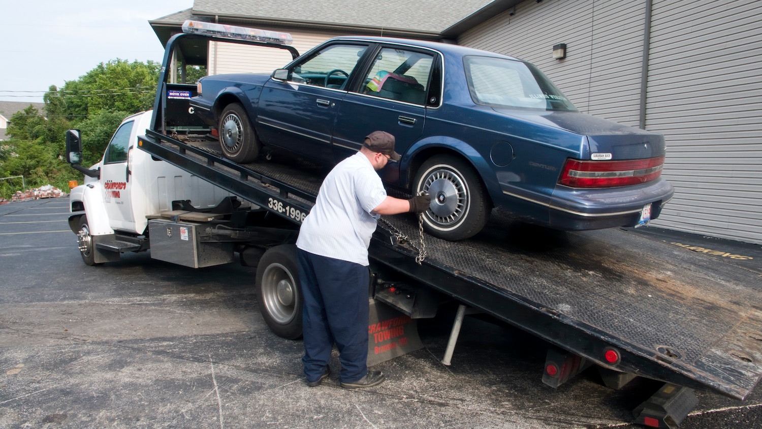 Dark blue fifth-generation Buick Century four-door sedan loaded onto the flatbed of a tow truck