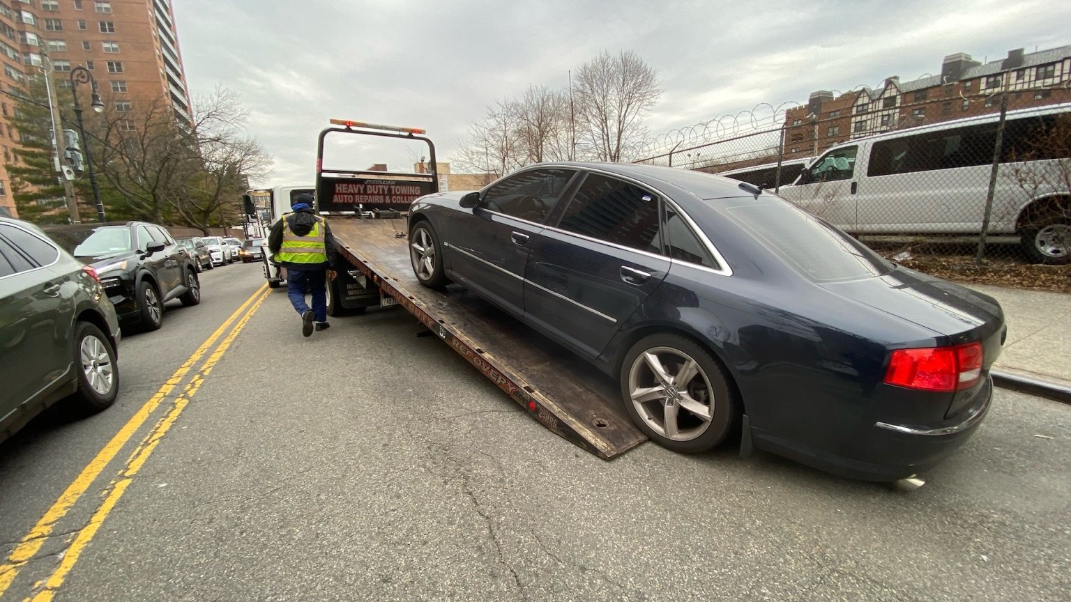 Dark-colored Audi A8 luxury sedan loaded onto the flatbed of a heavy-duty tow truck
