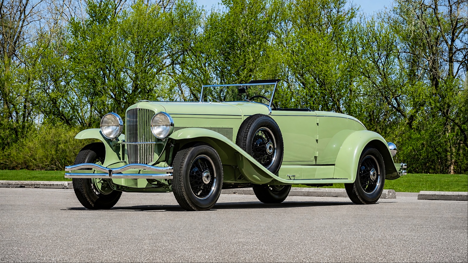 light green vintage Duesenberg is parked on a paved road.