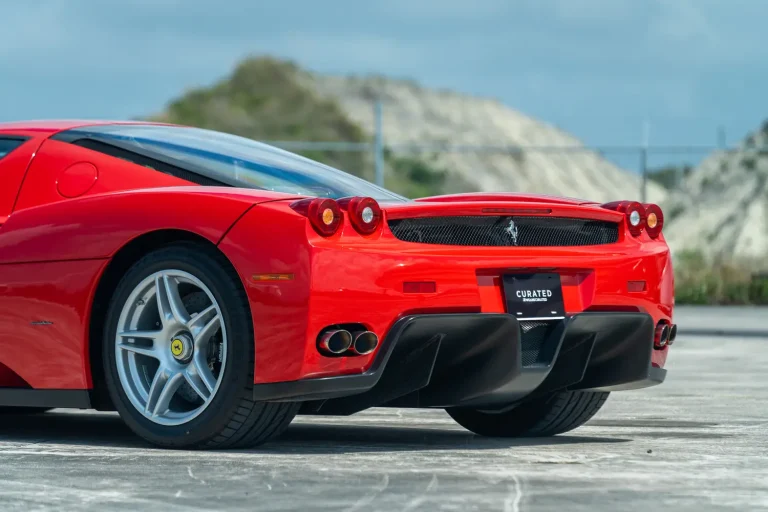 The back of a red Enzo Ferrari is shown on a road in front of a small hill