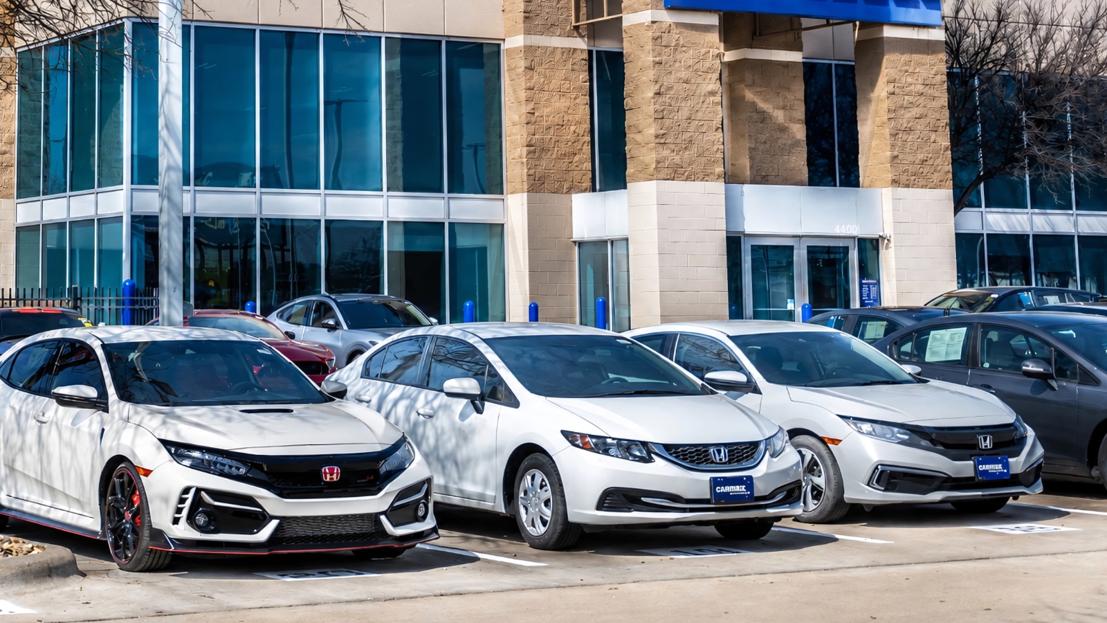 Several Honda cars parked neatly in a row outside a modern glass building