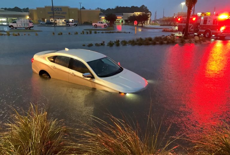 white sedan is stranded and partially submerged in a flooded parking lot at night