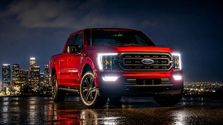 red Ford F-150 pickup truck parked at night with a city skyline backdrop