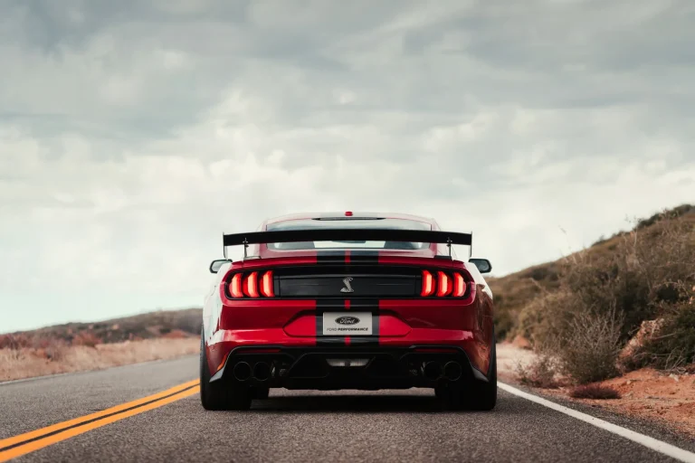 Rear view of a red Ford Mustang Shelby GT500 driving on an open desert highway