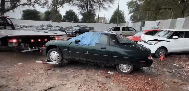 A dark green General Motors EV1 loaded onto a tow truck outdoors.