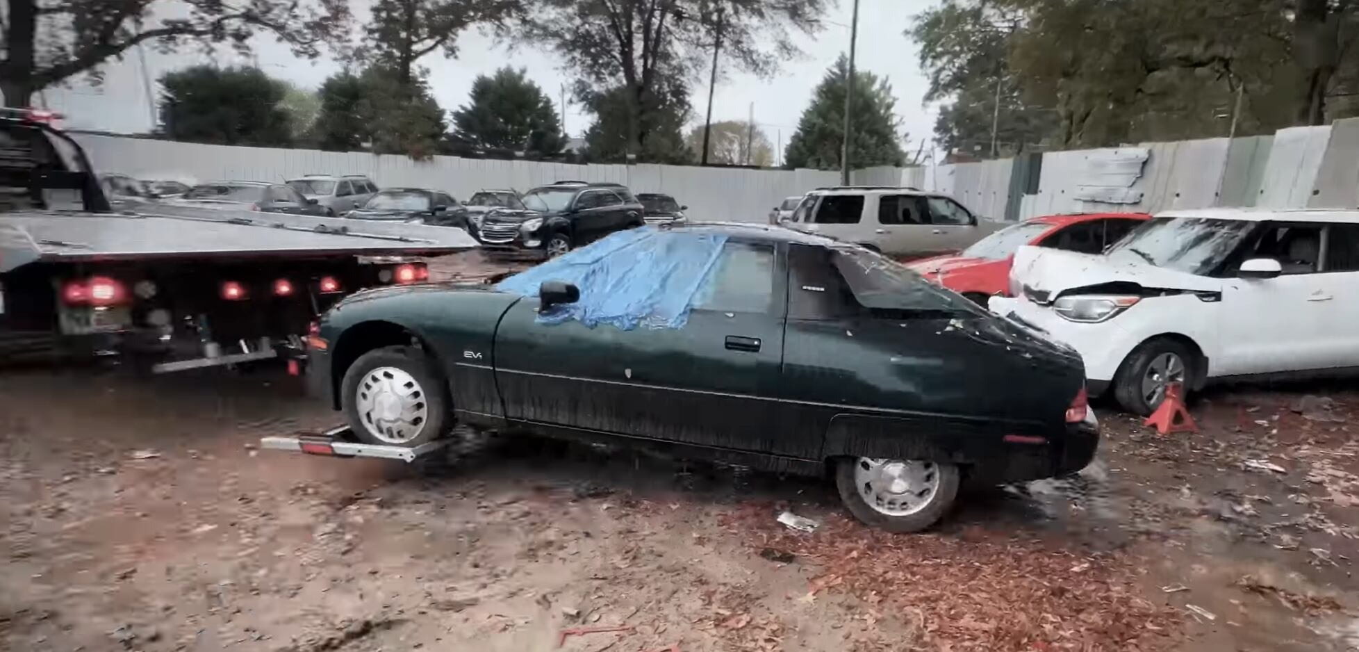 A dark green General Motors EV1 loaded onto a tow truck outdoors.