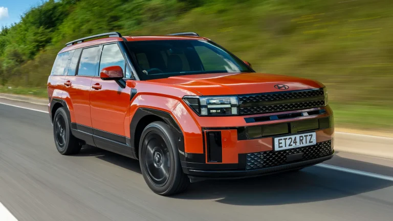 An orange Hyundai SUV driving fast along a scenic paved highway on a sunny day