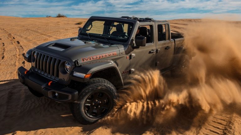dark gray Jeep Gladiator Mojave kicking up sand while driving across a desert
