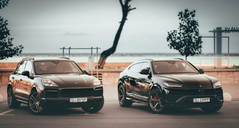 Two luxury black SUVs parked side by side near water