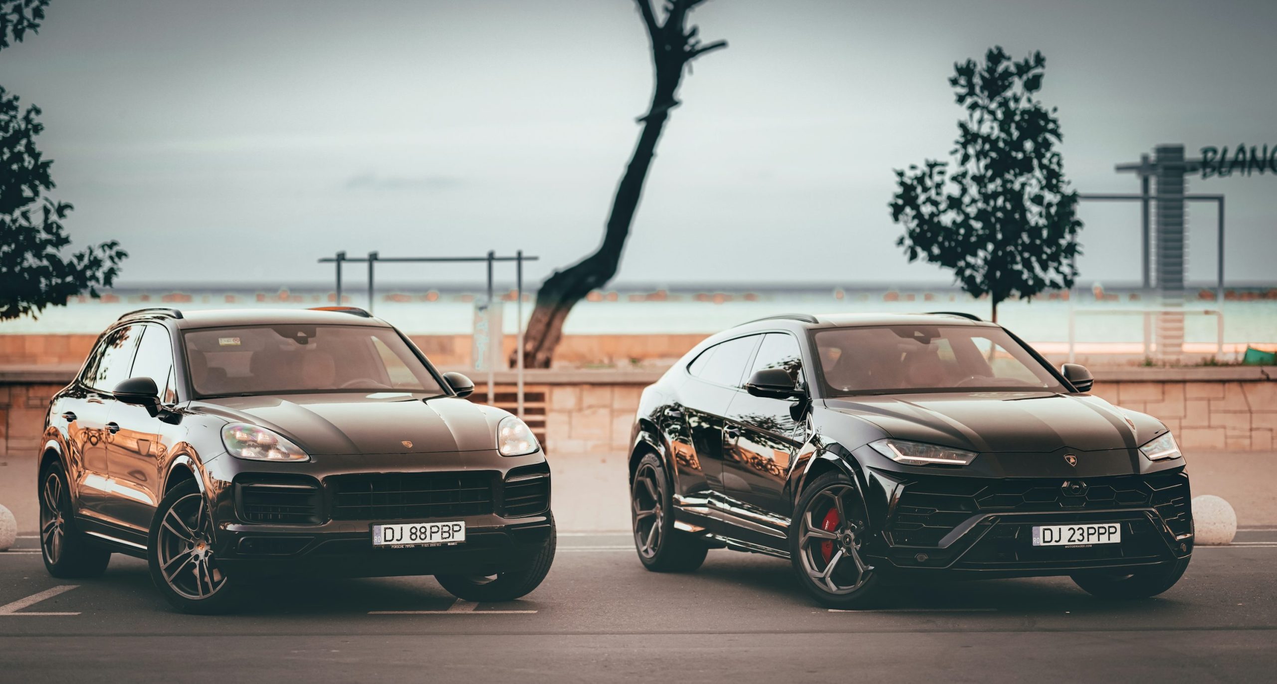 Two luxury black SUVs parked side by side near water