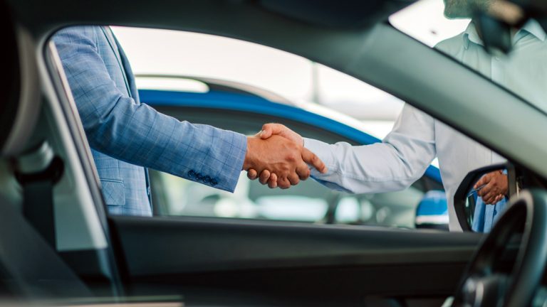 2 people are shaking hands near a car