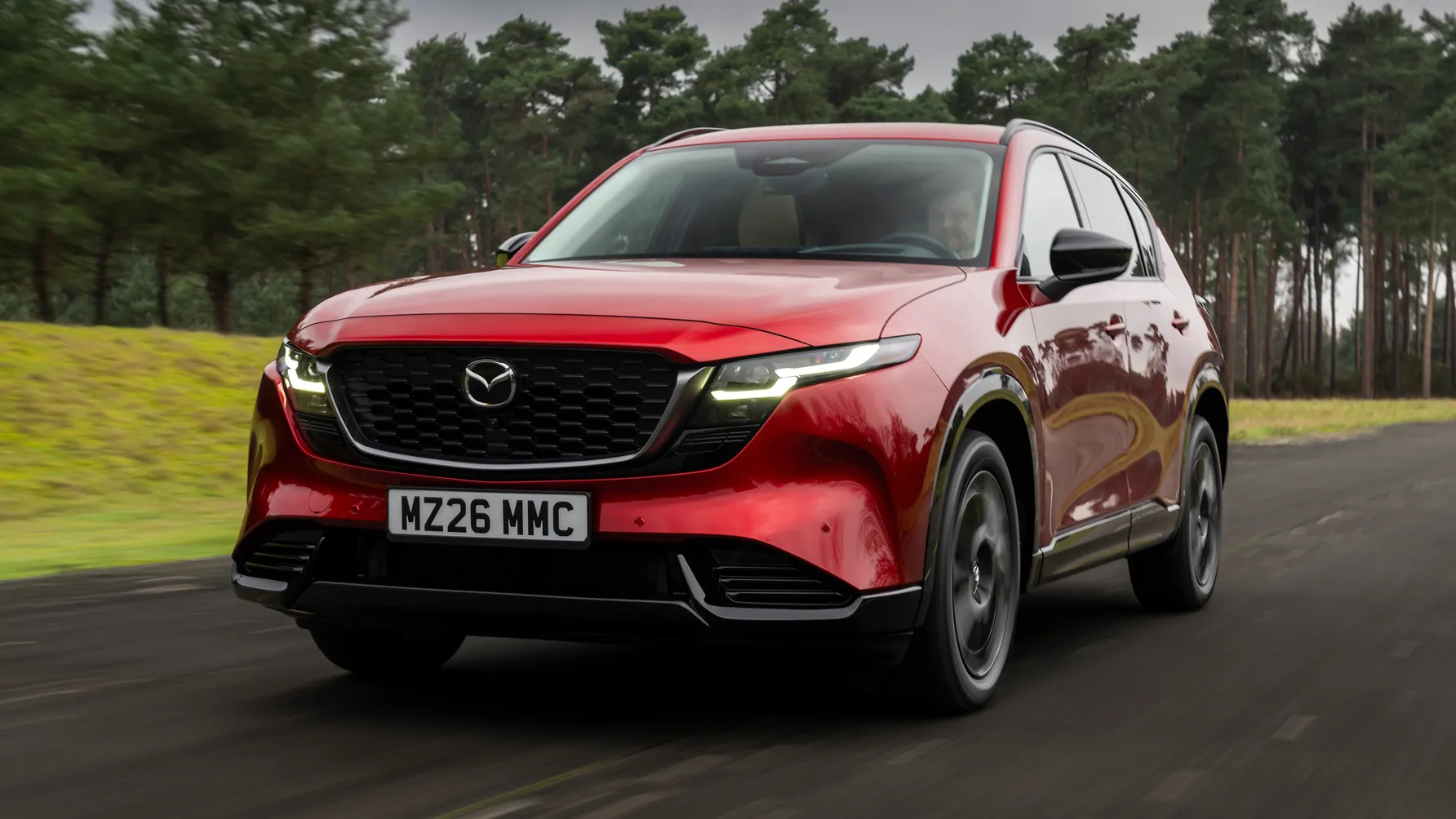 A red Mazda CX 5 standing on the side of a road beside the grass
