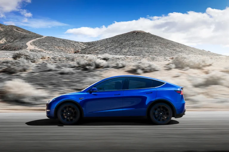 A blue Tesla Model Y speeding on a hilly highway
