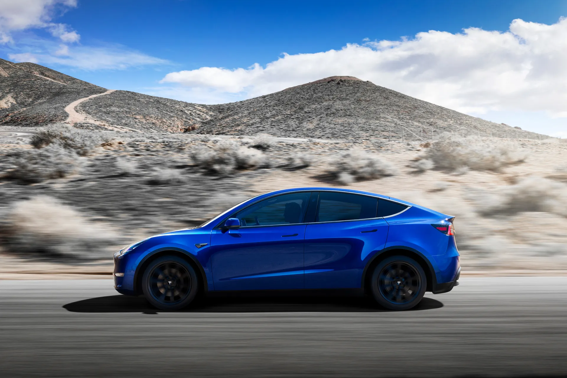 A blue Tesla Model Y speeding on a hilly highway