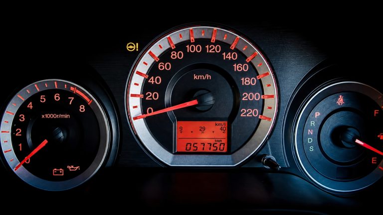 Car dashboard gauges showing speedometer, tachometer, fuel gauge, and warning light