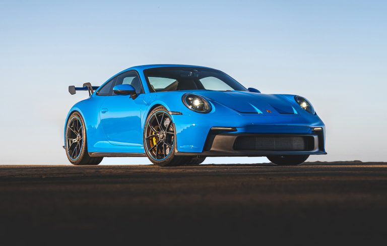 A blue Porsche 911 is standing still on a silent road