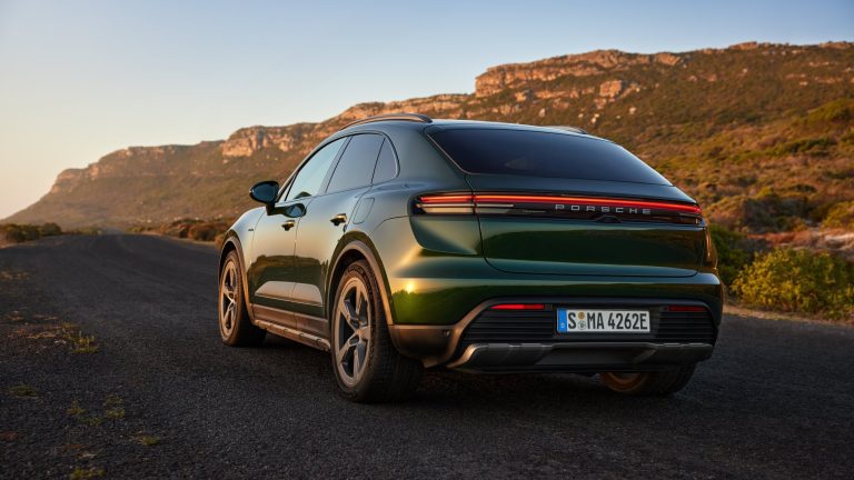 A dark green Porsche SUV parked on a winding asphalt road against rocky cliffs