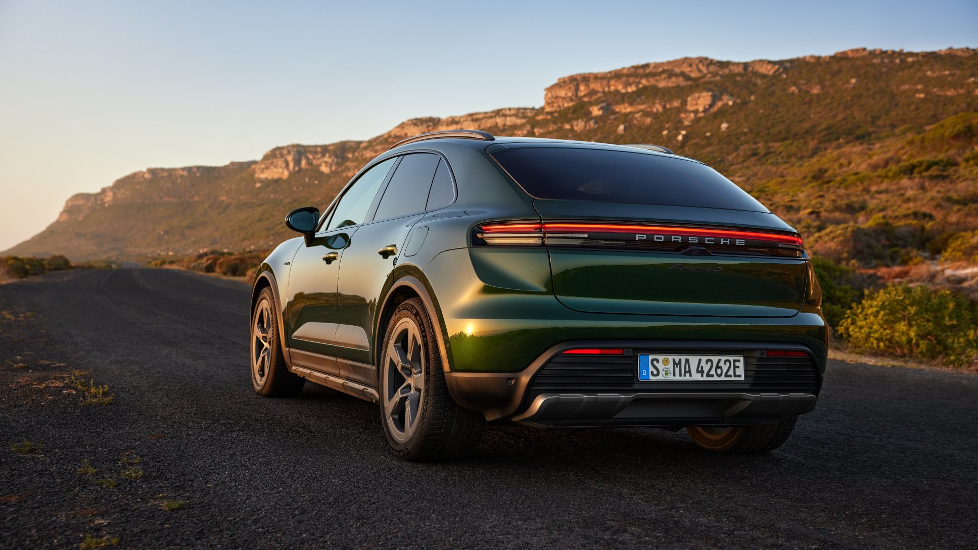 A dark green Porsche SUV parked on a winding asphalt road against rocky cliffs