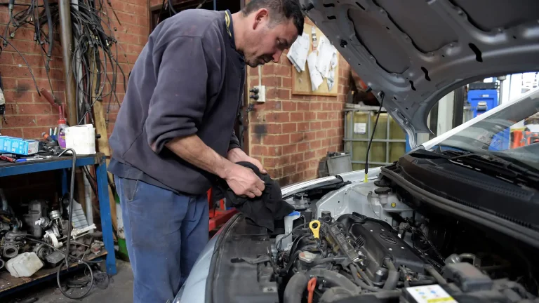 mechanic in a blue shirt cleaning his hands next to a car engine
