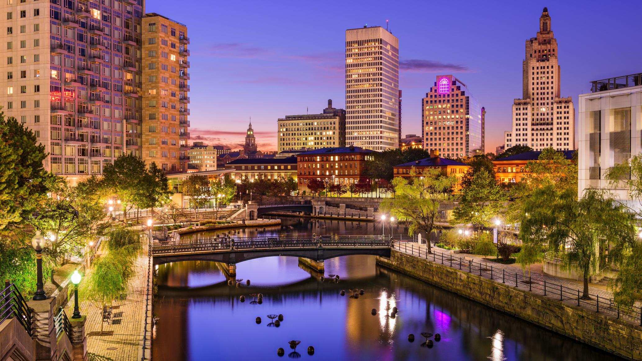 Illuminated city skyline along a river with bridges at dusk
