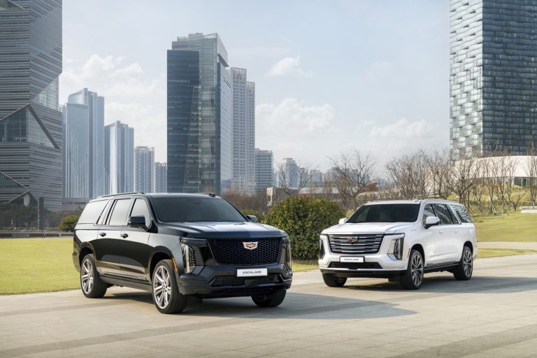 A black and a white Cadillac Escalade parked outdoors against a modern city skyline