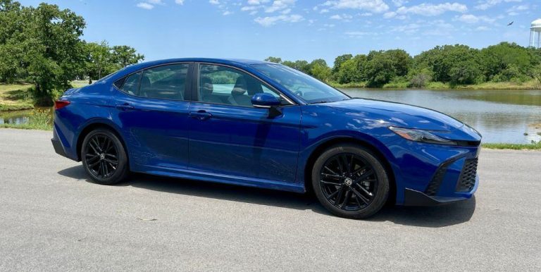 A sleek blue sedan parked on a paved road next to a scenic lake