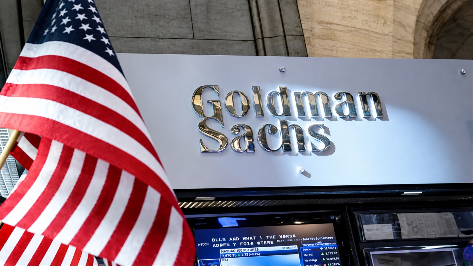A Goldman Sachs sign appears behind an American flag inside a financial market setting