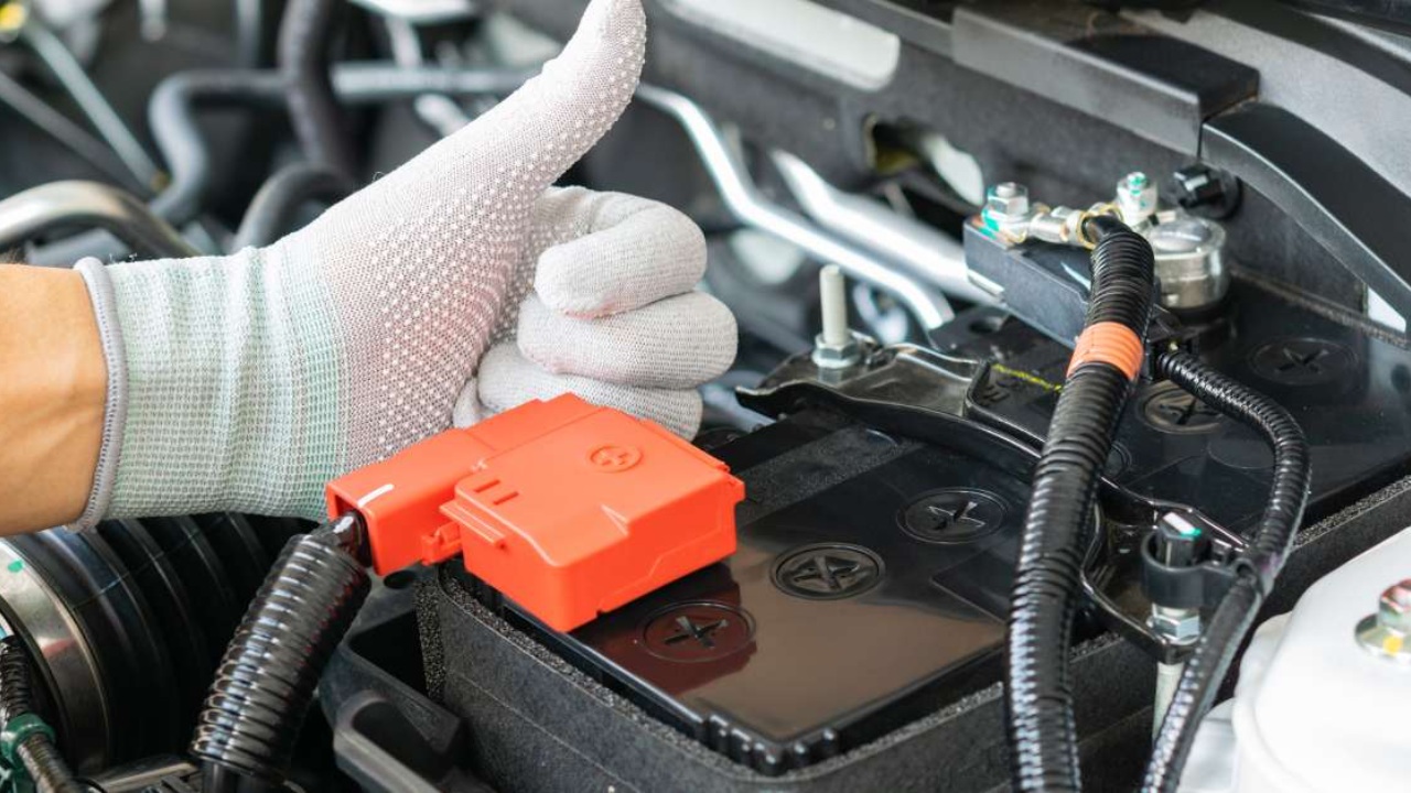A mechanic checks a car battery and electrical connections inside an engine bay