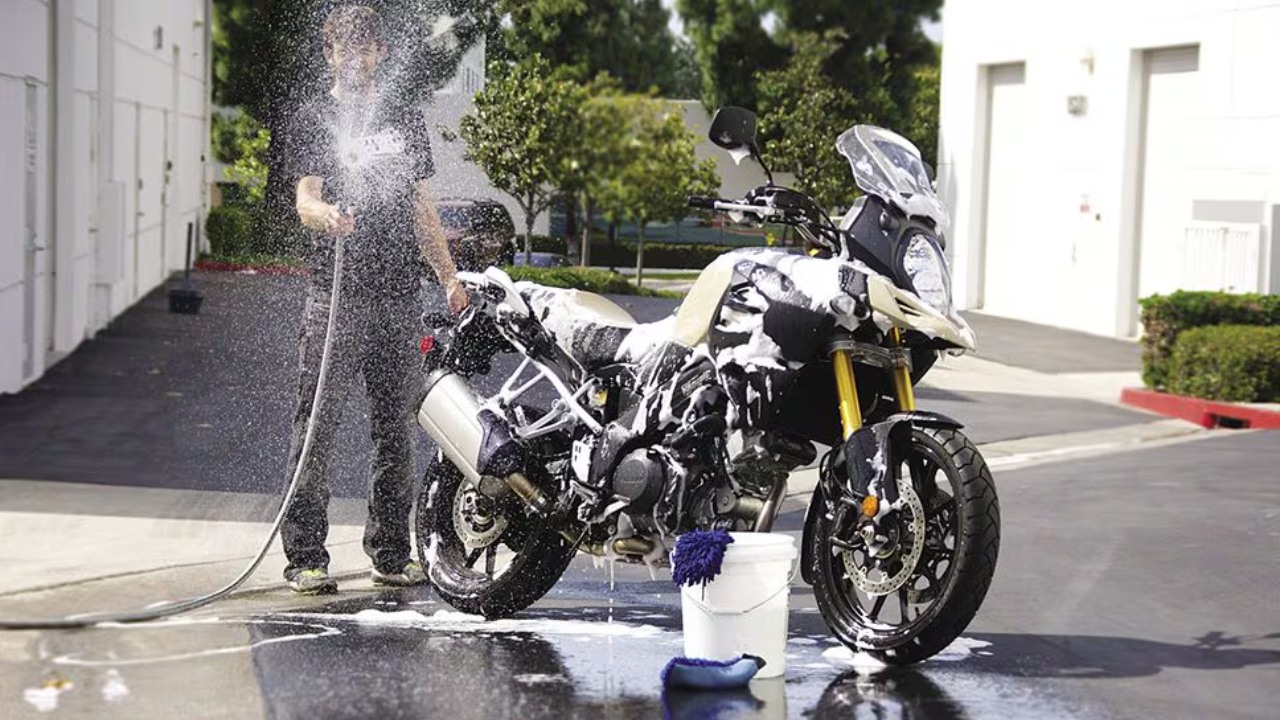 A person washes a motorcycle with soap and water outdoors