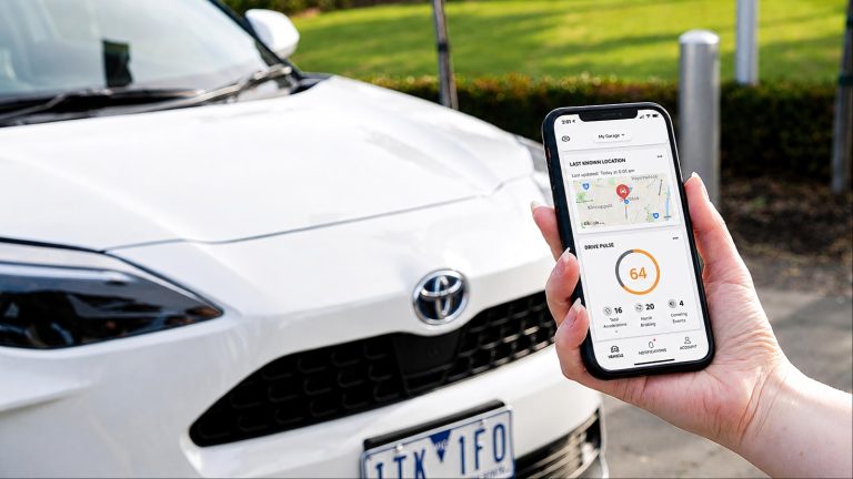 A smartphone showing connected-car data beside a Toyota vehicle