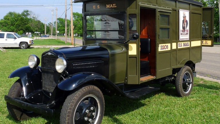 A vintage U.S. Mail truck parked on grass beside a roadway