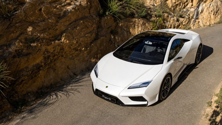 A white Lotus sports car parked on a winding mountain road beside a rocky hillside