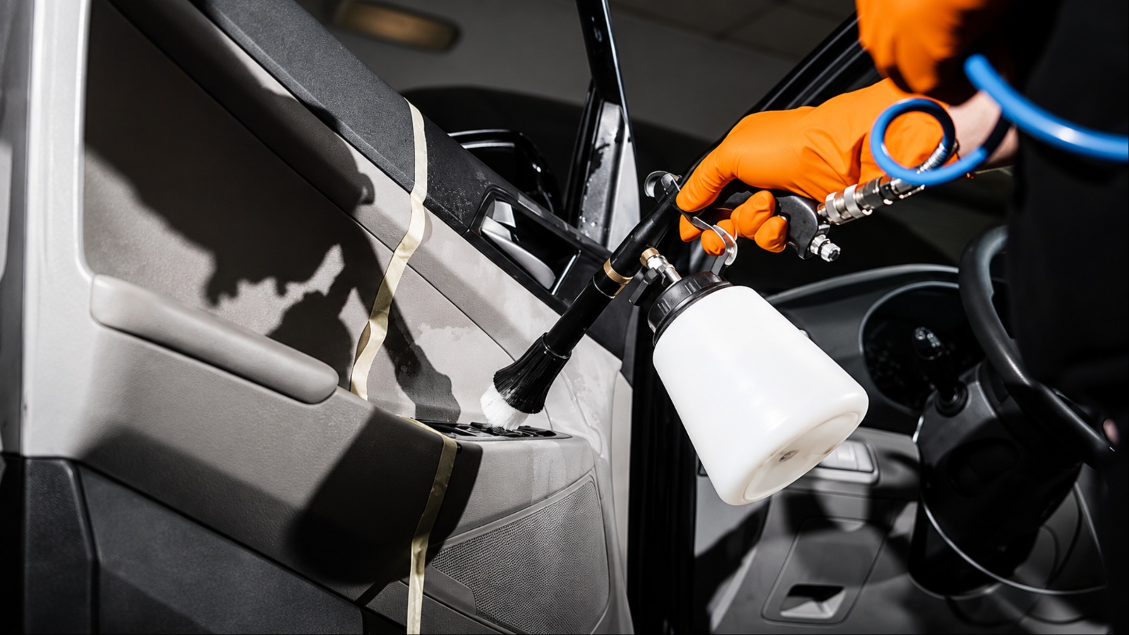 A worker uses a spray gun to clean a vehicle’s interior door panel
