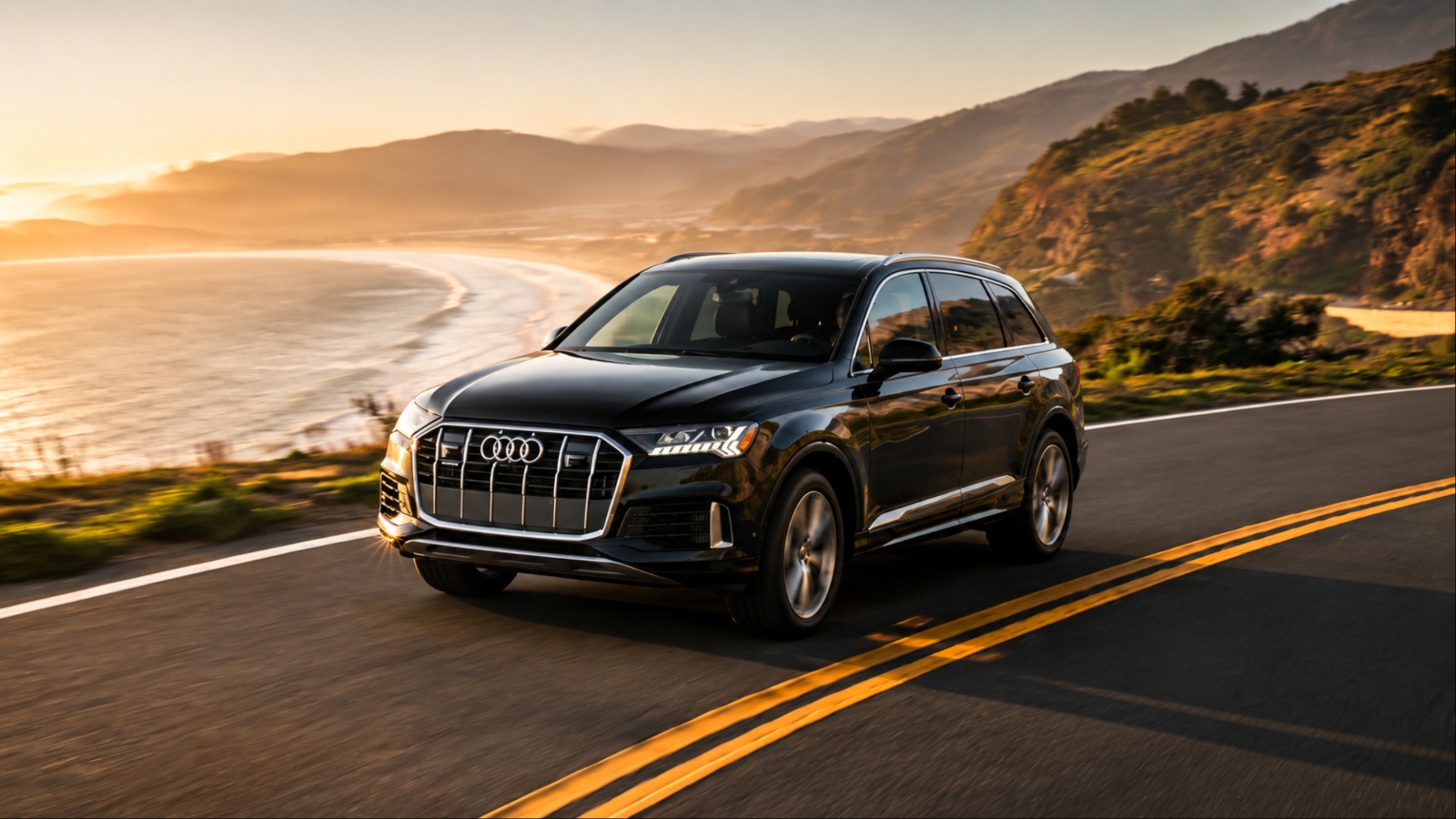 Black Audi Q7 drives along a scenic mountain road at sunset
