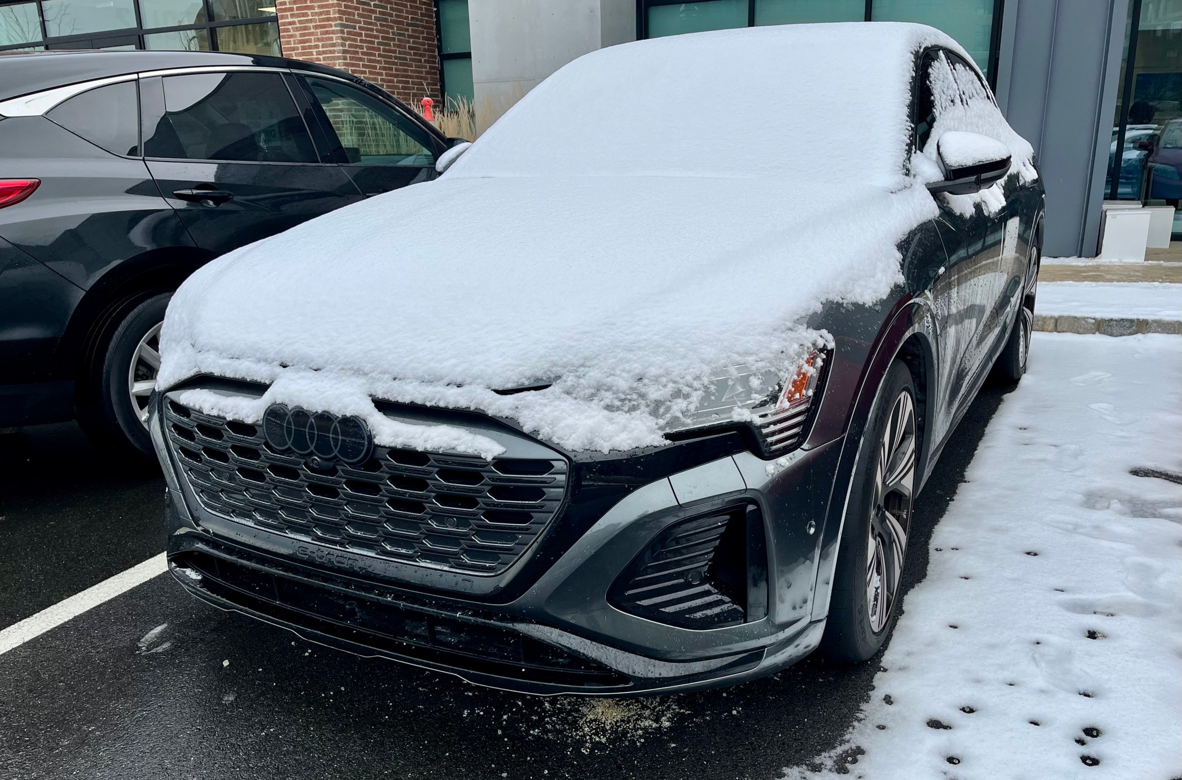 dark gray Audi Q8 e-tron parked outdoors, covered with a layer of fresh snow