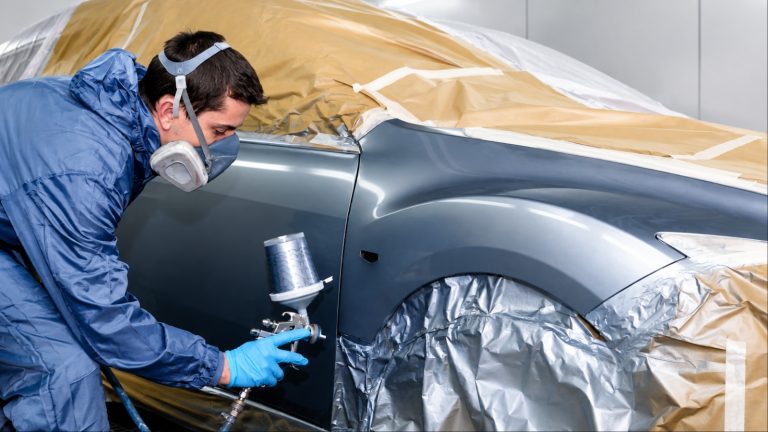 Auto painter in respirator mask spray-painting a masked car body