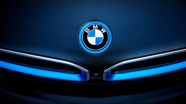 Close-up of the BMW logo above the illuminated front grille of a dark blue BMW.