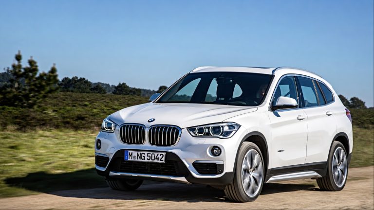 BMW X1 driving along a scenic rural road under clear blue skies