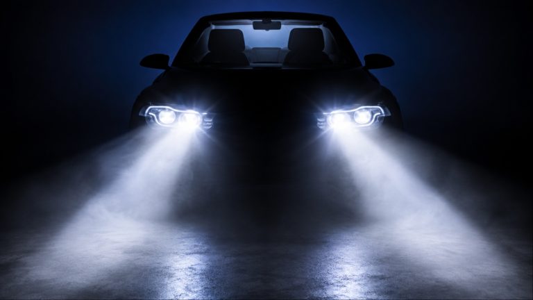 Car headlights illuminating a dark road at night with bright beams