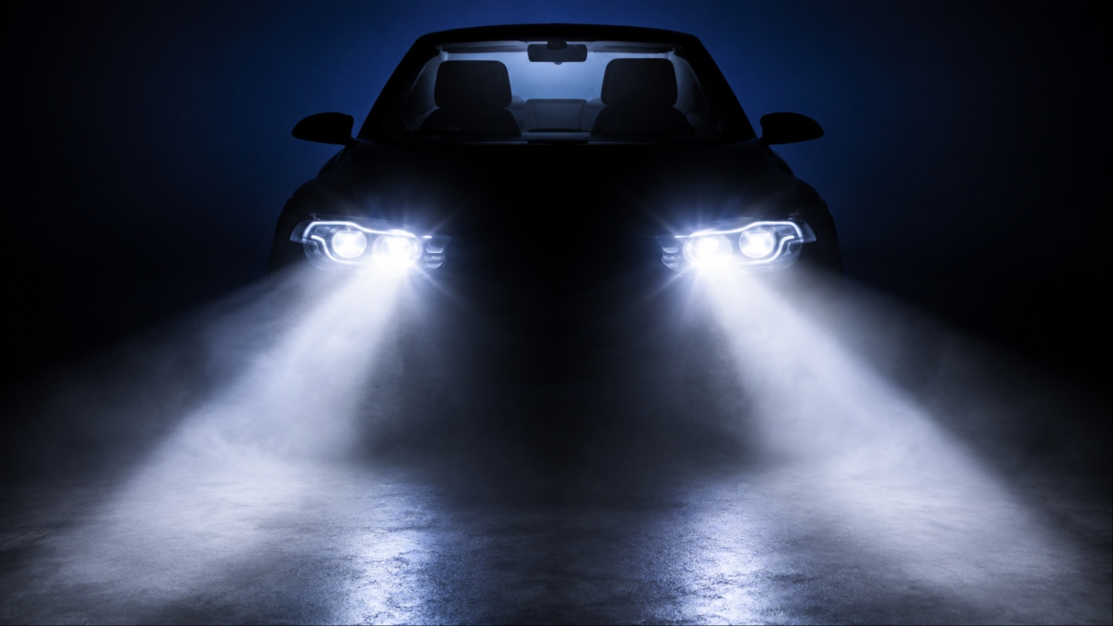 Car headlights illuminating a dark road at night with bright beams