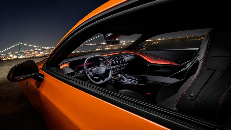 An orange car's interior featuring black leather seats and ambient lighting overlooking a lit bridge at night