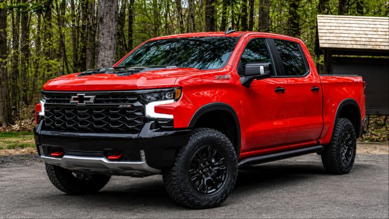 shiny red Silverado is standing in front of forest trees